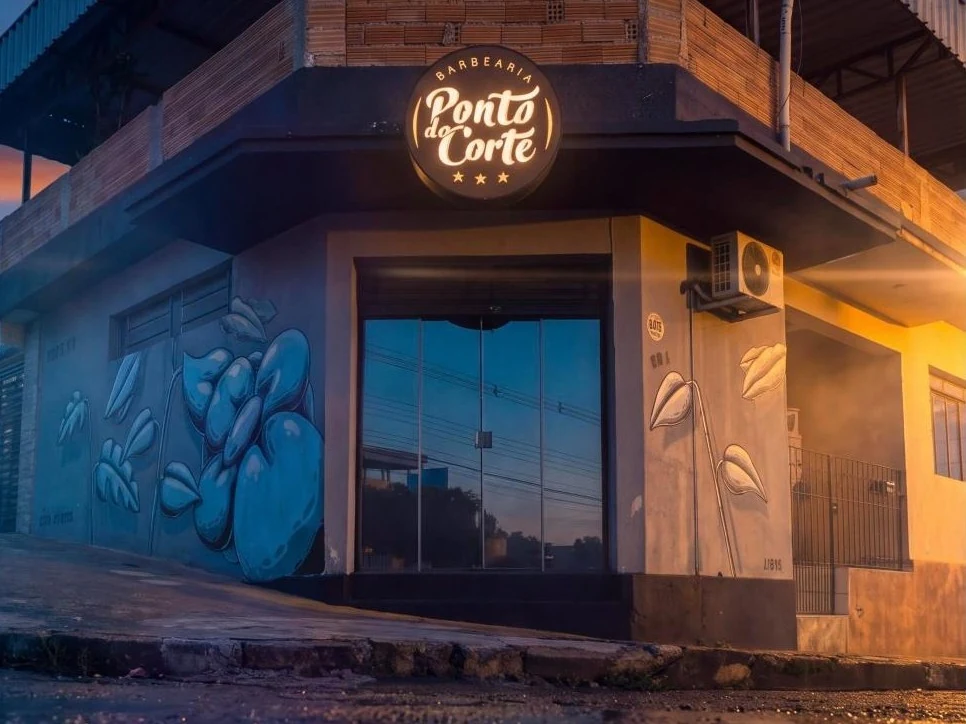 Fachada da Barbearia Ponto do Corte ao entardecer, com a placa acesa